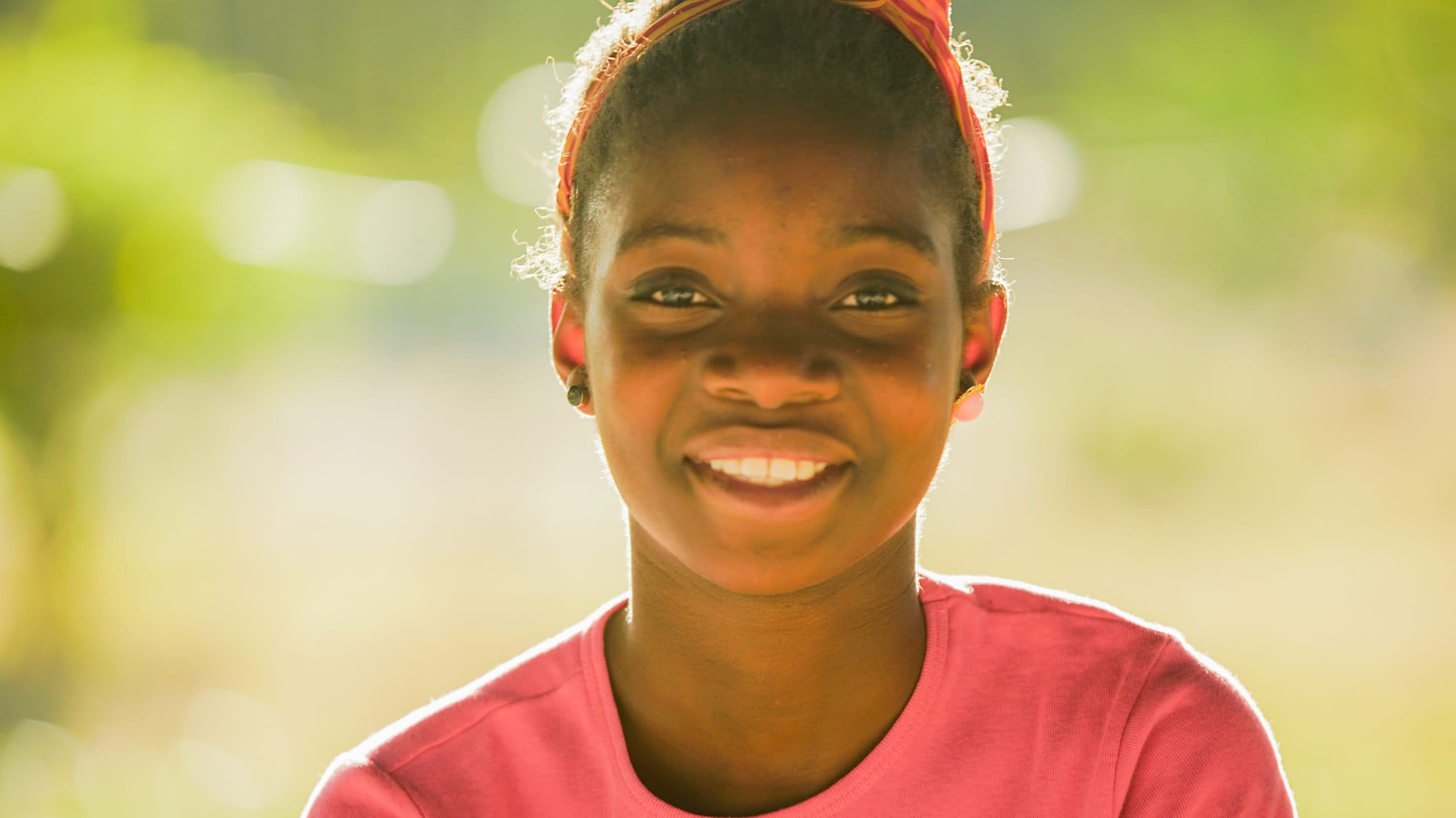 Zambian girl wearing pink and smiling in front of a green background outside.