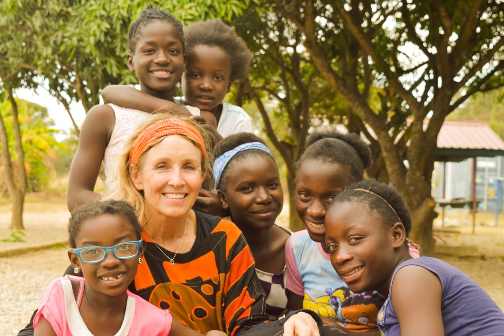 Kathy Headlee, smiling with a group of girls in Zambia underneath mango trees.