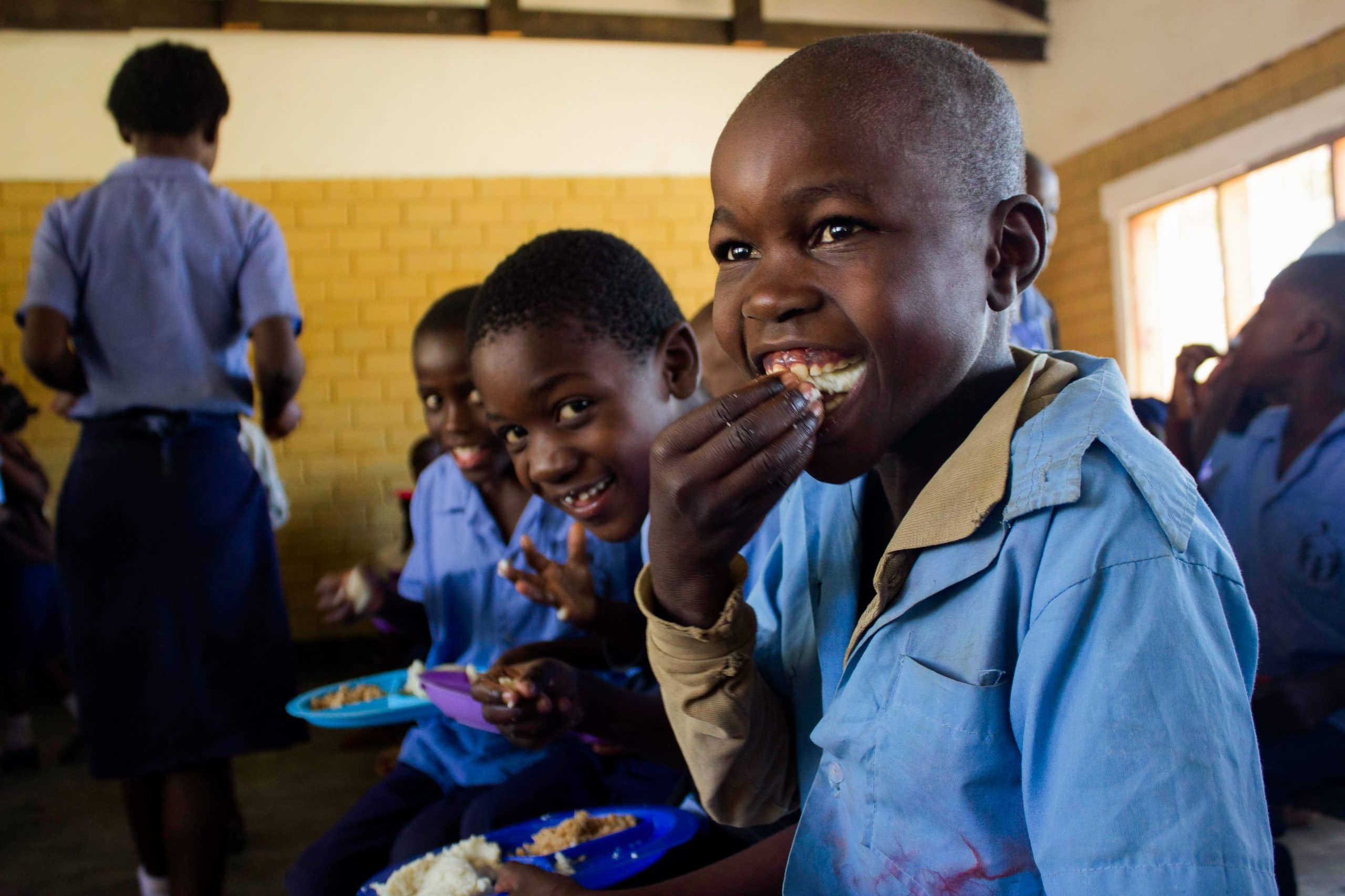 School kids in Zambia sitting on a bench and eating Zambia's staple food: Shima.