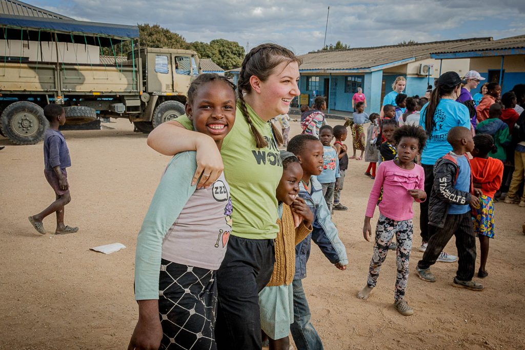 Volunteer in Zambia walking and smiling with her arms around three Zambian children.