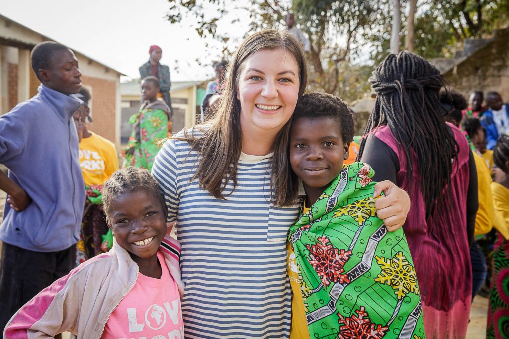 Volunteer in Zambia smiling with her arms around two little girls.