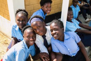 Girls in Zambia smiling wearing their school uniforms and sitting on the porch of the school.