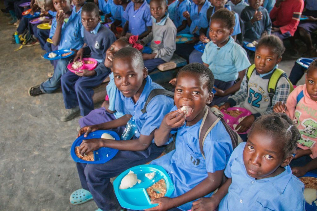 A group of school kids in Zambia eating lunch on benches.