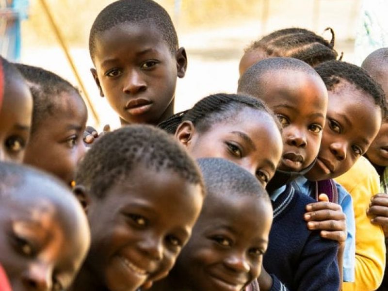 Kids in Zambia leaning in a row to look at the camera.
