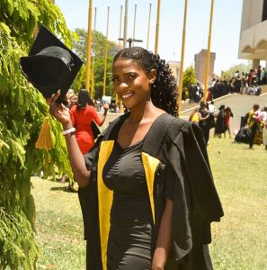 Zambian woman wearing a graduation cap and gown and smiling.