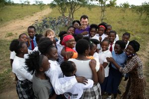Tanner, Kathy, and Josephine smiling and hugging a group of girls in Zambia.