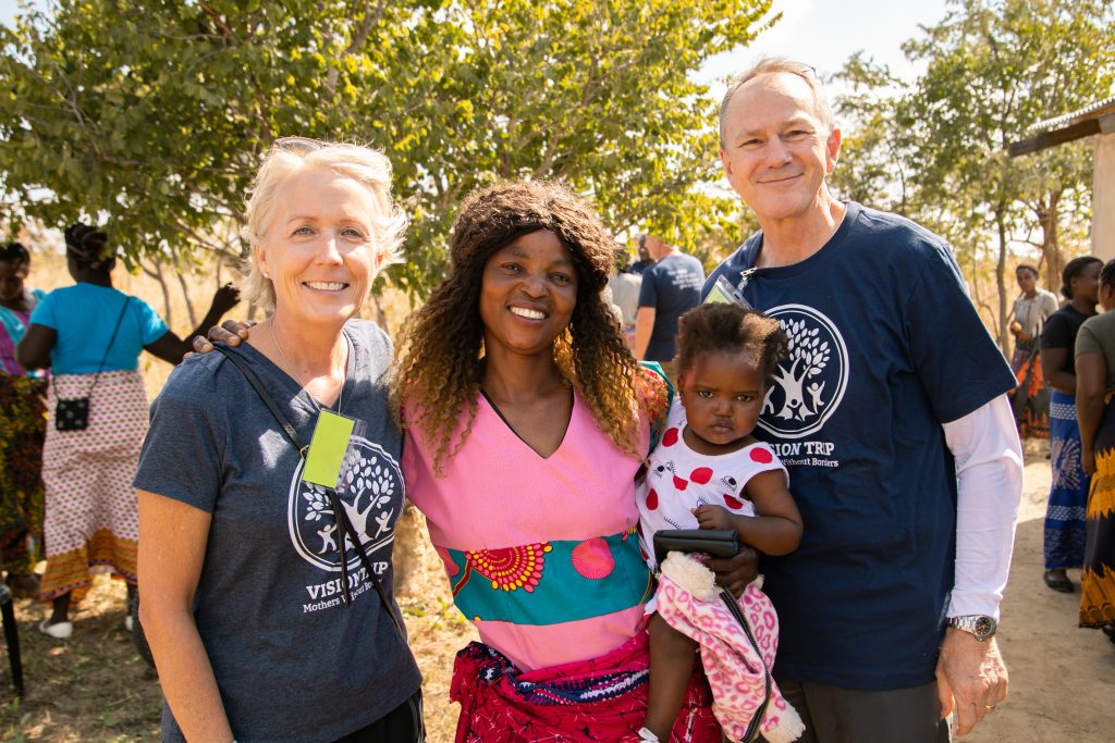 Woman with a baby smiling in between Melissa and Joel Gardner in Zambia.