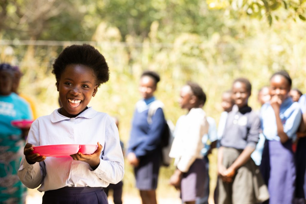 Little Zambian school girl smiling with her plate of food.