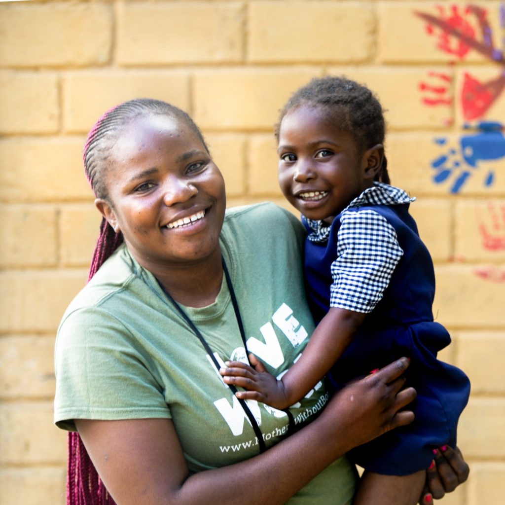 Woman in Zambia holding a young school girl and both of them smiling.