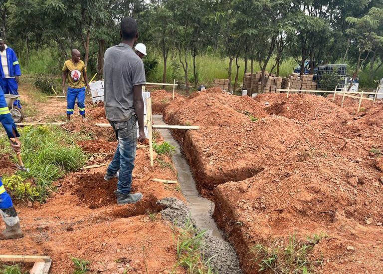 Zambian construction workers pouring cement footings in the dirt for the new buildings.