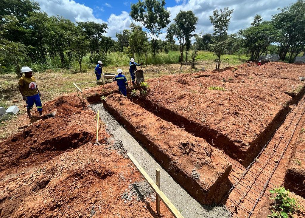 Zambian workers pouring cement out of a wheelbarrow into the footings.