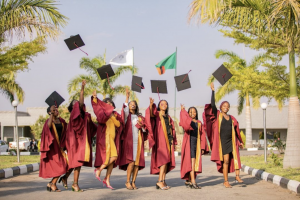Zambian girls standing in a line wearing graduation gowns and throwing their caps into the air.